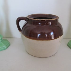 Op de afbeelding: Een bruine en witte geglazuurde keramische pot met een handvat. De pot heeft een bruine bovenkant en een witte onderkant.