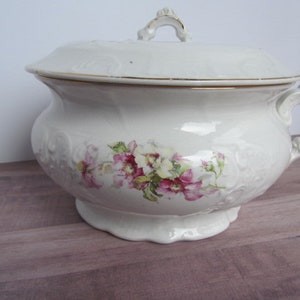 Puede incluir: Olla de cerámica blanca con tapa y diseño floral. La olla tiene un borde dorado alrededor de la parte superior y un asa en el lateral.