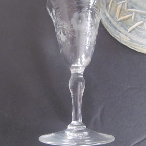 May include: A clear, etched glass with a floral design. The glass has a slender stem and a wide, flat base. The etched design includes a flower and leaves. The glass is likely for serving a beverage.