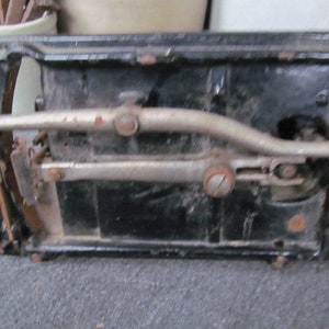 Op de afbeelding: Close-up van de onderkant van een vintage zwarte naaimachine met een zilveren metalen hendel en een zilveren metalen arm.