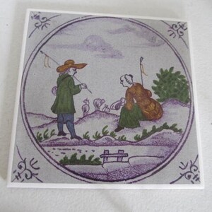 May include: A vintage tile with a hand-painted scene of two figures in a landscape. The figures are a man and a woman, both wearing traditional clothing. The man is holding a stick and the woman is holding a basket. There are sheep in the background.