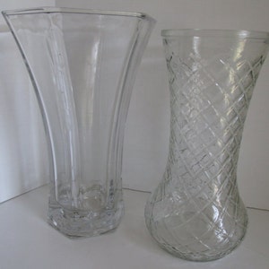 May include: Two clear glass vases. The vase on the left is tall and slender with a flared top. The vase on the right is shorter and wider with a diamond pattern.