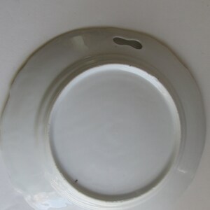 May include: White ceramic plate with a scalloped edge and two holes on either side. The plate is designed for serving food.