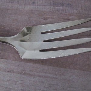 Puede incluir: Un tenedor de plata con cuatro dientes. El tenedor está hecho de metal y tiene un acabado pulido.