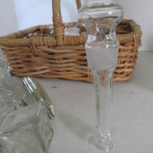 May include: A set of clear glass bottle stoppers with a frosted finish. The stoppers are in a wicker basket.