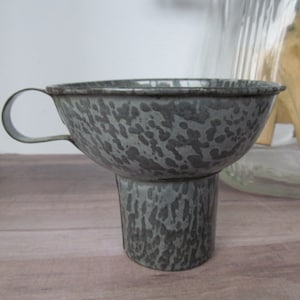 May include: A gray enamel funnel with a handle. The funnel has a speckled pattern and a wide, round opening.