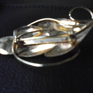 May include: A gold-toned leaf-shaped brooch with a pin closure on the back. The brooch has a textured surface and a delicate design.