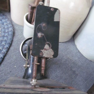 Op de afbeelding: Een vintage zwarte naaimachine met een metalen basis en een zwarte metalen arm. De machine heeft een naald en een spoelhouder.