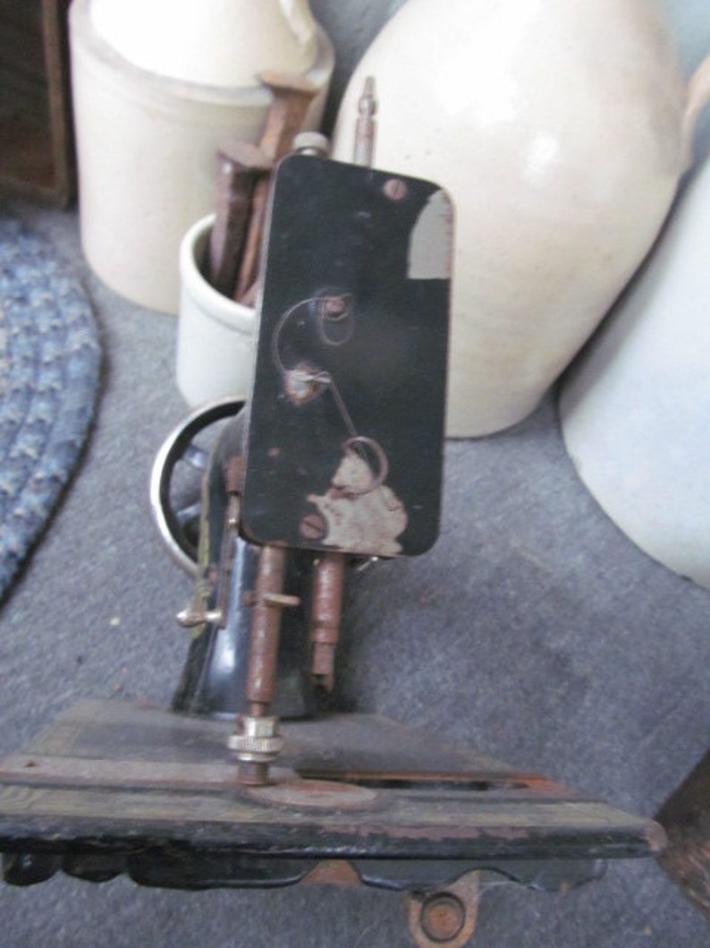 Op de afbeelding: Een vintage zwarte naaimachine met een metalen basis en een zwarte metalen arm. De machine heeft een naald en een spoelhouder.