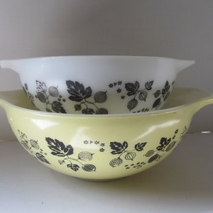 May include: Two vintage Pyrex mixing bowls, one white and one yellow, with a black and white gooseberry pattern. The bowls are nested together.