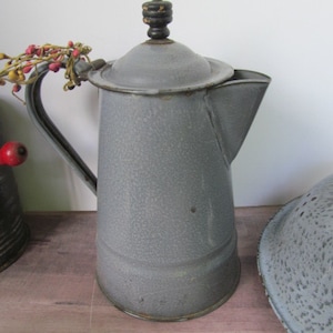 May include: A gray enamel coffee pot with a black wooden knob on the lid. The pot has a speckled gray finish and a spout on the side.