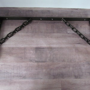 May include: Two black metal brackets with a chain connecting them. The brackets are L-shaped and have a rustic finish.