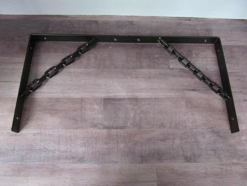 May include: Two black metal brackets with a chain connecting them. The brackets are L-shaped and have a rustic finish.