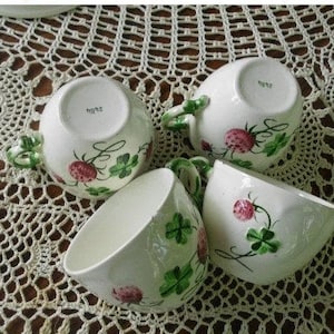 May include: Four white teacups with green clover and pink strawberry designs. The cups have the text "hg12" on the bottom.
