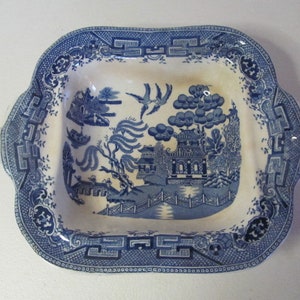 May include: A blue and white porcelain serving dish with a willow pattern design. The dish has a square shape with rounded corners and a raised rim.
