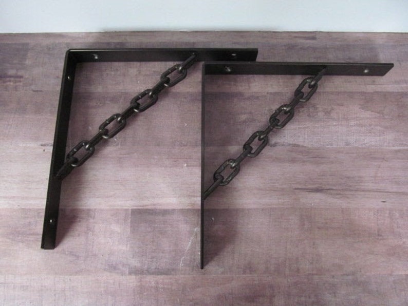 May include: Two black metal shelf brackets with a chain design. The brackets are angled and have a rustic look.