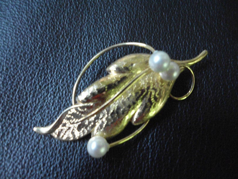 May include: A gold leaf brooch with two white pearls. The leaf is textured and has a delicate wire design.