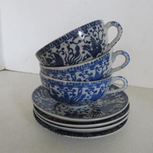 May include: A stack of four blue and white porcelain teacups and saucers with a floral and bird design.
