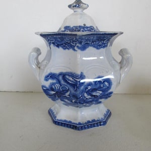 Puede incluir: Un azucarero de porcelana blanca con un diseño floral azul y blanco. El tazón tiene una tapa y dos asas.