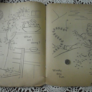 May include: A vintage connect-the-dots activity book with two pages. The left page shows a girl in a kitchen setting with the text "What am I doing?" The right page shows a boy flying a kite with the text "Windy day fun."