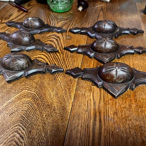 May include: Six intricately carved wooden knobs with a starburst design. The knobs are dark brown and have a rustic finish.