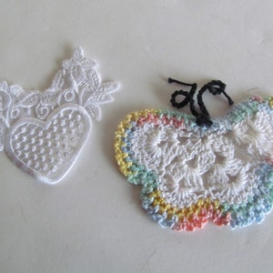 May include: Two white lace appliques, one shaped like a heart with floral details and the other shaped like a butterfly with a rainbow border.