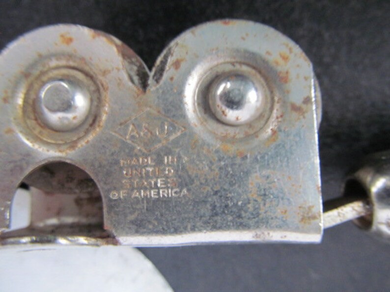 Puede incluir: Un abrelatas de plata con mango negro. El abrelatas tiene dos ruedas y el texto "ASO" y "MADE IN THE UNITED STATES OF AMERICA" est&aacute; impreso en el lateral.
