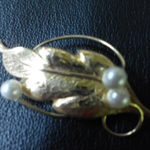 May include: A gold leaf brooch with three white pearls. The leaf is textured and has a delicate wire design.