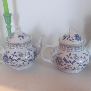 May include: Two white teapots with blue and white floral designs. The teapots have a lid and a spout.