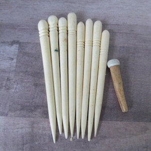 Könnte beinhalten: Satz von acht weißen Stricknadeln aus Holz mit einer einzelnen Holzstricknadel mit weißer Spitze.
