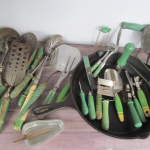 Puede incluir: Una colecci&oacute;n de utensilios de cocina vintage con mangos verdes. Los utensilios incluyen una variedad de herramientas, como un machacador de patatas, un batidor, una esp&aacute;tula, un rallador y una cuchara. Los utensilios est&aacute;n dispuestos en una sart&eacute;n de hierro fundido.