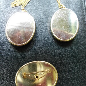 May include: Three gold-toned oval-shaped pendants with a chain. Two of the pendants are on chains and the third pendant has a pin on the back.