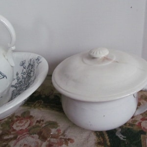 Puede incluir: Un orinal de cerámica blanca con tapa y asa. El orinal tiene un diseño sencillo y está decorado con un patrón floral.