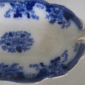 May include: A white oval serving dish with a blue and white floral pattern. The dish has a scalloped edge and a gold trim.