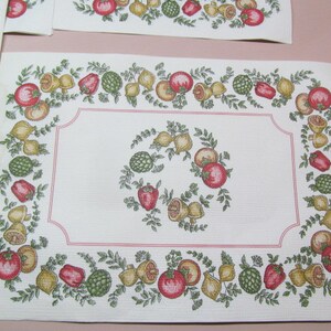May include: White placemat with a red, green, and yellow border of fruit and vegetables. The center of the placemat is white with a red border.