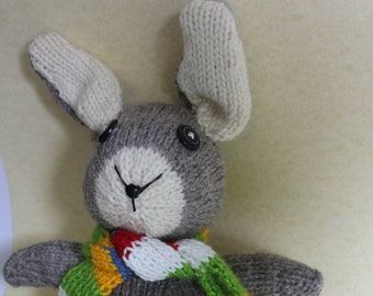 May include: A gray knitted bunny rabbit wearing a colorful striped scarf. The bunny has black button eyes and a black button nose.