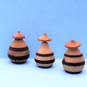 Puede incluir: Tres pequeños frascos de madera, con tapa, de forma redondeada, rayados de marrón y negro.