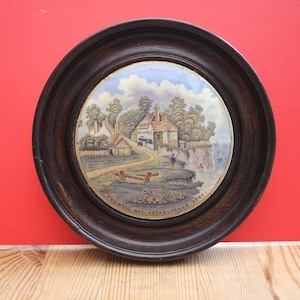 May include: A circular painting in a dark wooden frame, showing a coastal landscape with buildings and figures. The painting includes the text "PEGWELL BAY ESTABLISHED 1760". The frame is dark brown and circular.