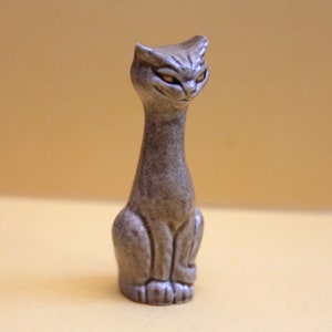 May include: A ceramic figurine of a grey cat with a long neck and a sitting pose. The cat has a textured surface and a slightly menacing expression.