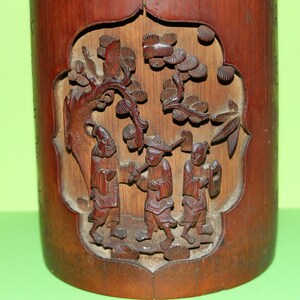 May include: A carved wooden cylinder depicting a scene of three figures in a woodland setting. The figures are carved in relief and appear to be wearing traditional Chinese clothing. The cylinder is made of dark wood and has a smooth, polished finish.
