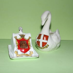 May include: Two porcelain figurines, one a swan with a red and white crest and the other a butter dish with a crest featuring a building and the words "Sherborne Abbey".