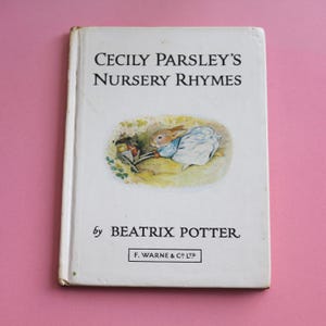 May include: A white book with the title "Cecily Parsley's Nursery Rhymes" by Beatrix Potter. The cover features an illustration of a rabbit in a blue dress pushing a wheelbarrow.