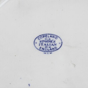 May include: Close-up of a white ceramic plate with a blue oval stamp. The stamp reads "Copeland Spode's Italian England" in a circular arrangement. The plate has a smooth, glossy surface.