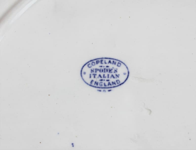 May include: Close-up of a white ceramic plate with a blue oval stamp. The stamp reads "Copeland Spode's Italian England" in a circular arrangement. The plate has a smooth, glossy surface.