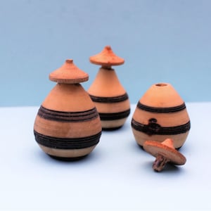 May include: Three small, wooden, pear-shaped containers with black and brown striped patterns. Each container has a small, round, wooden lid.