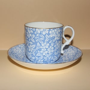 Puede incluir: Un juego de taza y platillo de té azul y blanco. La taza tiene un delicado patrón floral y un borde dorado. El platillo combina con la taza.