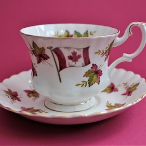 May include: A white teacup and saucer with a gold rim. The teacup has a red and white Canadian flag design with maple leaves.