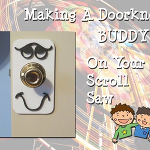 May include: A white wooden door knob with a black face drawn on it. The door knob is a gold color. The text "Making A Doorknob Buddy On Your Scroll Saw" is in the upper right corner of the image.