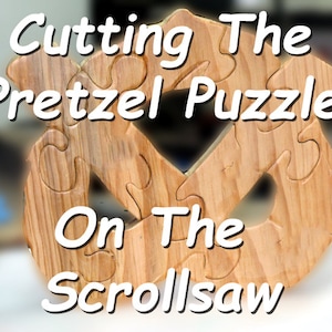 Könnte beinhalten: Ein Holz-Brezel-Puzzle, das auf einer Laubsäge geschnitten wird. Das Puzzle ist aus hellem braunem Holz gefertigt und hat eine natürliche Holzoptik. Der Text "Cutting The Pretzel Puzzle On The Scroll Saw" ist in Weiß auf einem verschwommenen Hintergrund geschrieben.