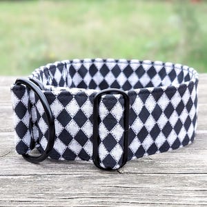 May include: A black and white dog collar with a diamond pattern. The collar has black metal hardware and is made of a sturdy fabric. The collar is designed for a medium to large dog.
